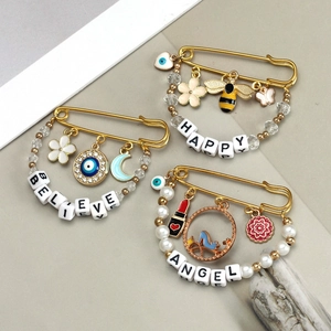 Detailed view of three golden pins with Evil Eye, Bee, and Happy/Believe letter beads