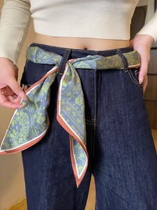 Close-up of a grey-green paisley silk scarf used as a waist belt on blue denim jeans