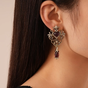 Close-up of vintage gold earrings with purple resin hearts and sparkling rhinestones