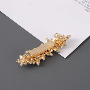 Detailed close-up of golden leaf-shaped metal hair clip with intricate textures