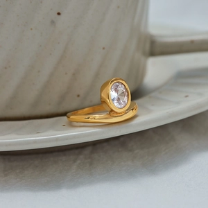 Elegant 18K gold plated stainless steel ring with an oval zircon on a white ceramic plate