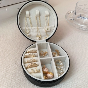 Detail of round black leather jewelry box with white velvet lining and gold accessories