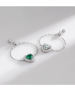 Macro detail of adjustable silver chain rings featuring emerald and clear heart-shaped gems