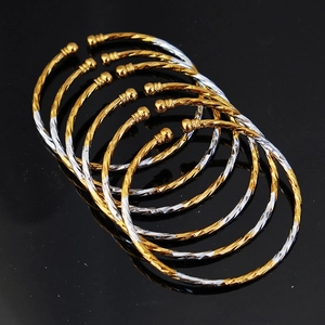 Detail of twisted gold and silver bangles with ball ends on a dark surface