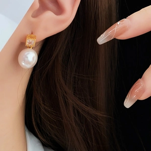 Close-up of gold-plated square gemstone and pearl stud earrings worn by a model
