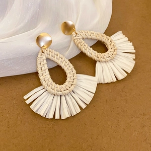 Detail of teardrop rattan woven earrings with cream fan tassels and gold hooks