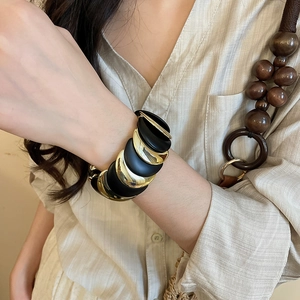Close-up of wide layered bracelet featuring alternating black and gold metal curves