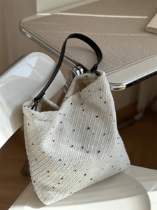 Detail of off-white tweed tote bag with colorful fibers hanging on a modern chair