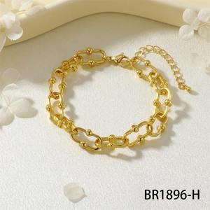 Dettaglio di un bracciale dorato a maglie a U con sfere metalliche e chiusura a moschettone