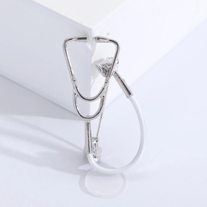 Close-up of a silver medical stethoscope brooch with white accents on a minimalist base