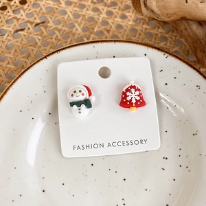 Macro shot of snowman and red snowflake bell Christmas stud earrings on a white card