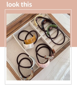 Detail of C-shaped acetate hair ties in marble and amber patterns in a wooden box