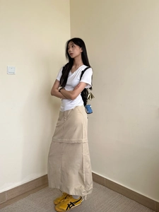 Detailed outfit view of white V-neck T-shirt paired with beige skirt and retro sneakers