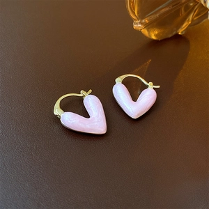 Macro de boucles d'oreilles cœur en émail rose et plaqué or sur un fond de cuir texturé