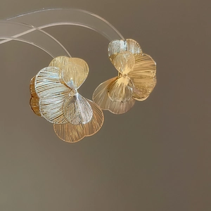 Vue détaillée de boucles d'oreilles fleur dorées avec pétales superposés et texture brossée