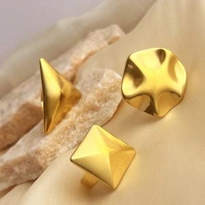 Three geometric 18K gold plated stainless steel rings displayed on silk fabric