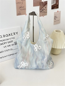 Detail of light blue mesh tote bag with 3D white floral embroidery on a vintage desk
