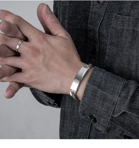 Close-up of a silver Cuban link bracelet with a rectangular plate and a minimalist ring