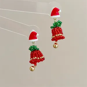 Macro shot of handmade beaded Christmas tree earrings with red bow and gold bell detail