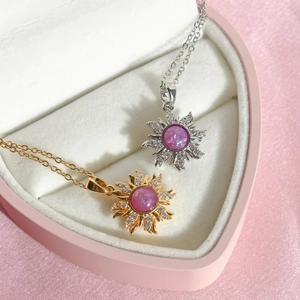 Close-up of gold and silver sunflower necklaces with pink opal in heart boxes