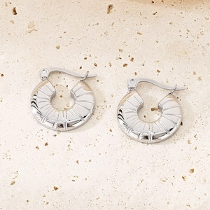 Détail macro de boucles d'oreilles créoles argentées avec texture rayonnante sur pierre