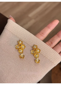 Macro detail of gold flower drop earrings featuring five crystal-studded floral petals