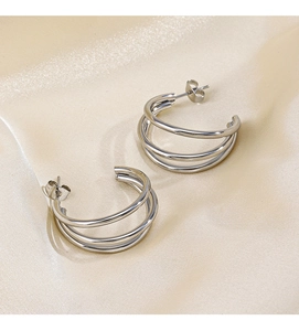 Detailed view of triple-layered C-shape silver earrings on elegant champagne silk fabric