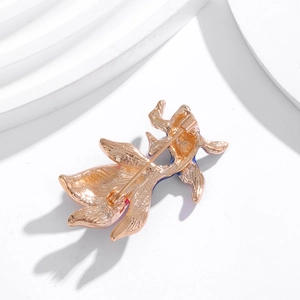 Back view of a gold goldfish brooch with enamel details on a minimalist white platform