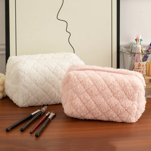 Close-up of fluffy pink and white quilted plush pencil cases on a wooden desk