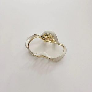 Close-up of irregular wave hair claw clip in creamy white enamel and gold metal finish