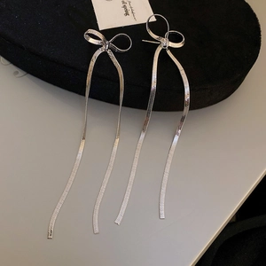 Detailed shot of long silver tassel bow earrings with metal chain on a black velvet stand