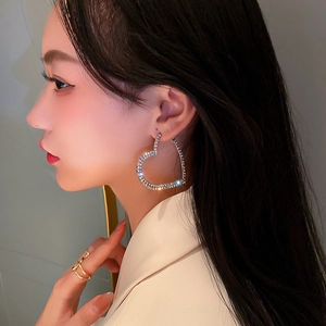 Vue latérale d'un mannequin portant de grandes boucles d'oreilles cœur argentées avec strass