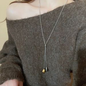 Macro shot of Y-shaped necklace with tiger eye stone and silver teardrop pendants on a sweater