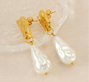 Macro detail of irregular gold metal stud and baroque pearl pendant on textured fabric