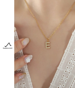 Close-up of a gold-plated stainless steel necklace with a crystal-studded letter E pendant