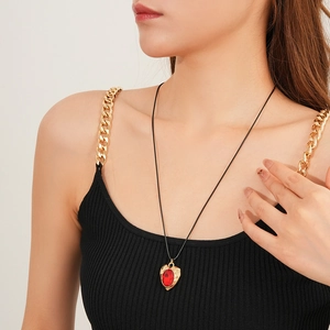 Close-up of vintage gold heart pendant with red crystal on a black rope chain