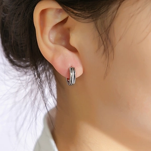 Gros plan d'une boucle d'oreille créole ondulée argent et noir portée sur le lobe