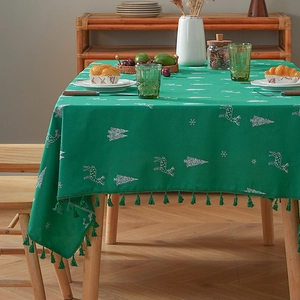 Green Christmas tablecloth with white deer embroidery and tassel fringe on a wooden table