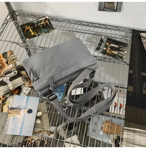 Detail of lightweight gray nylon crossbody bag displayed on a metal shelf with props