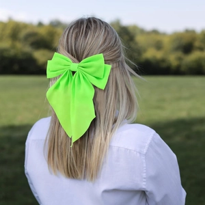 Detail of neon green oversized chiffon bow clip worn by a model in natural outdoor light