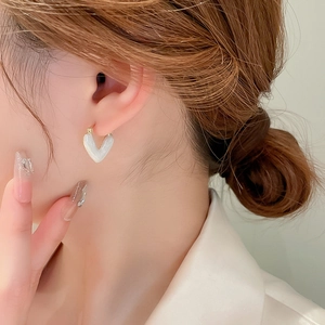 Detail of white enamel heart earring with gold plating shown on model ear