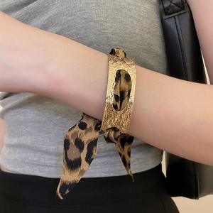 Close-up of golden hammered metal cuff bracelet with leopard print silk scarf ribbon
