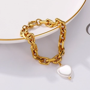 Detail eines Goldkettenarmbands mit weißem Herz-Perlenanhänger auf einem weißen Porzellanteller