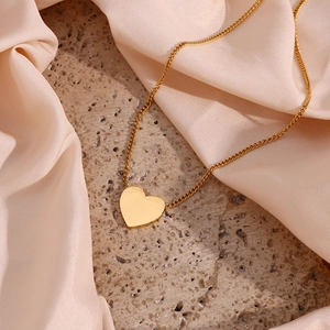 Detail of a polished gold heart pendant necklace on a soft pink satin background