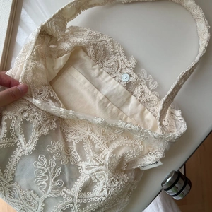 Detail of French lace embroidery on ivory shoulder bag with satin lining and magnetic clasp