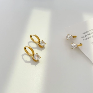 Detailed view of gold plated round and pear cut zircon earrings set on white background