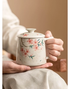 Detail of hand-painted peach blossom ceramic tea mug with lid held in a cozy setting