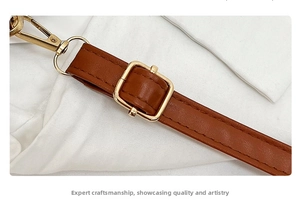 Close-up of brown leather shoulder strap with golden metal buckle and stitching detail