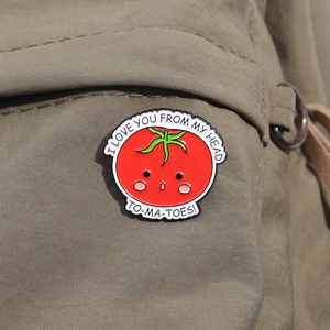 Close-up of a cute tomato enamel pin with I love you from my head tomatoes text