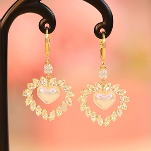 Detail of heart-shaped gold earrings with iridescent pearl inlay and marquise crystals